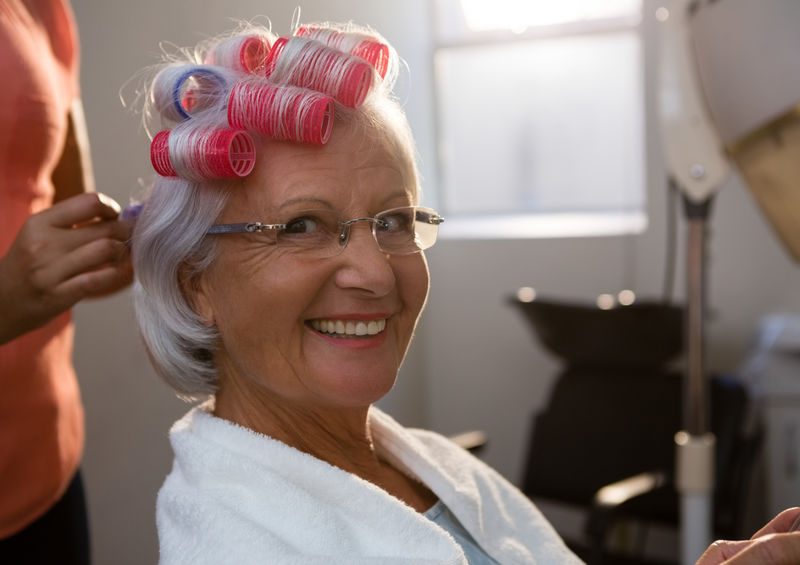 Cropped hands of hairstylist removing curlers from smiling senior woman hair